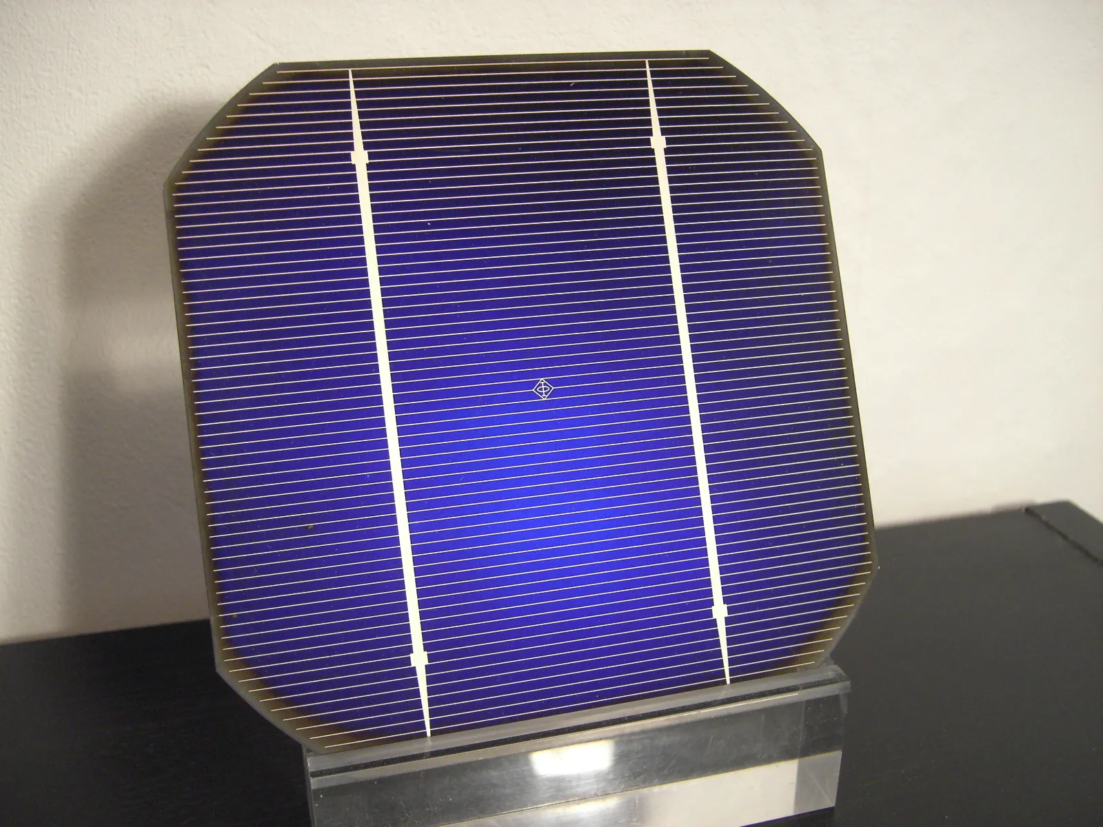 Cella fotovoltaica quadrata con gli angoli smussati, di colore blu, attraversata da due strisce metalliche verticali e da molte sottili righe orizzontali.
