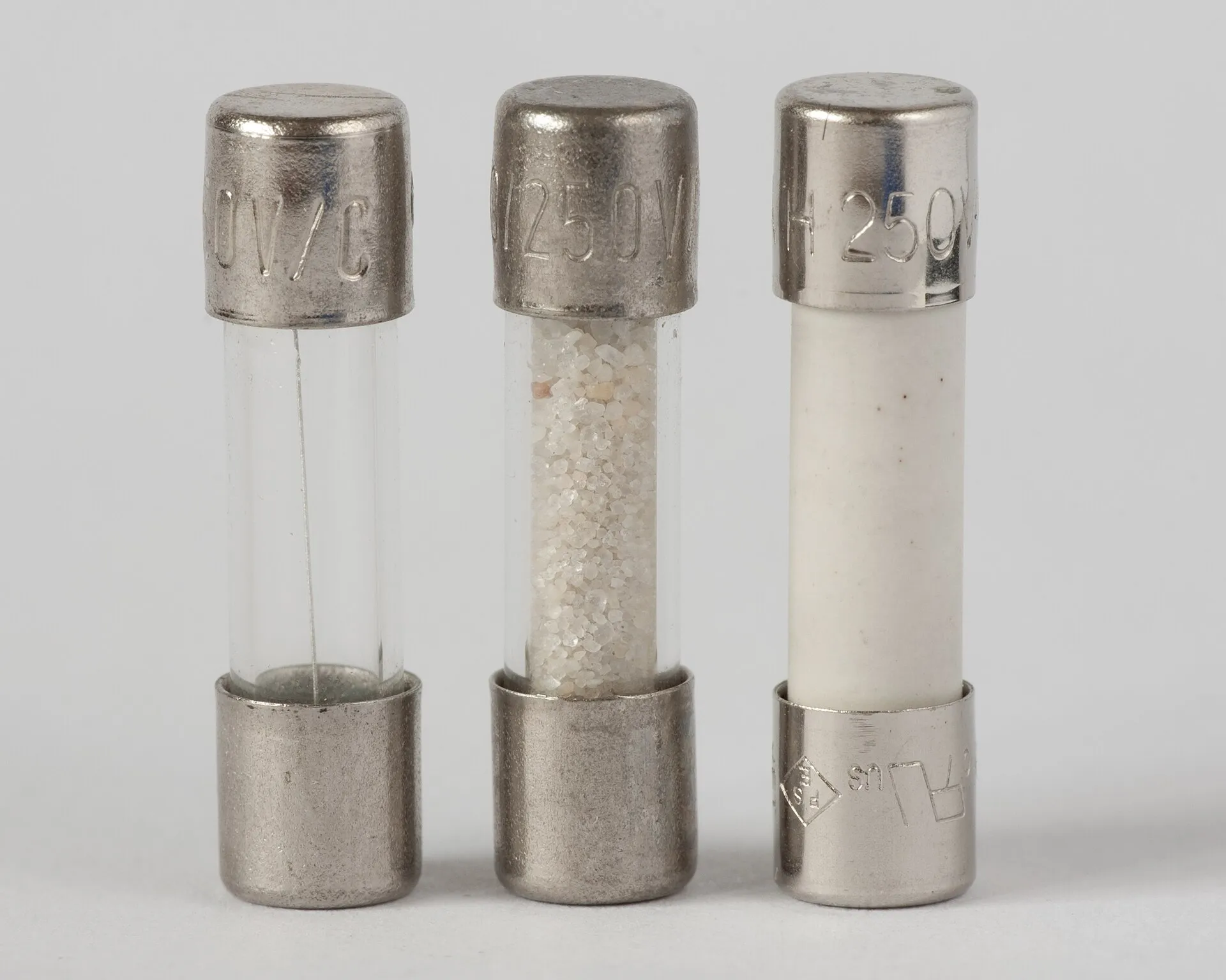 Tre fusibili cilindrici da 5 per 20 millimetri con cappucci metallici: il primo di vetro trasparente con un sottile filo teso all'interno, il secondo di vetro pieno di sabbia bianca, il terzo con il corpo di ceramica bianca.