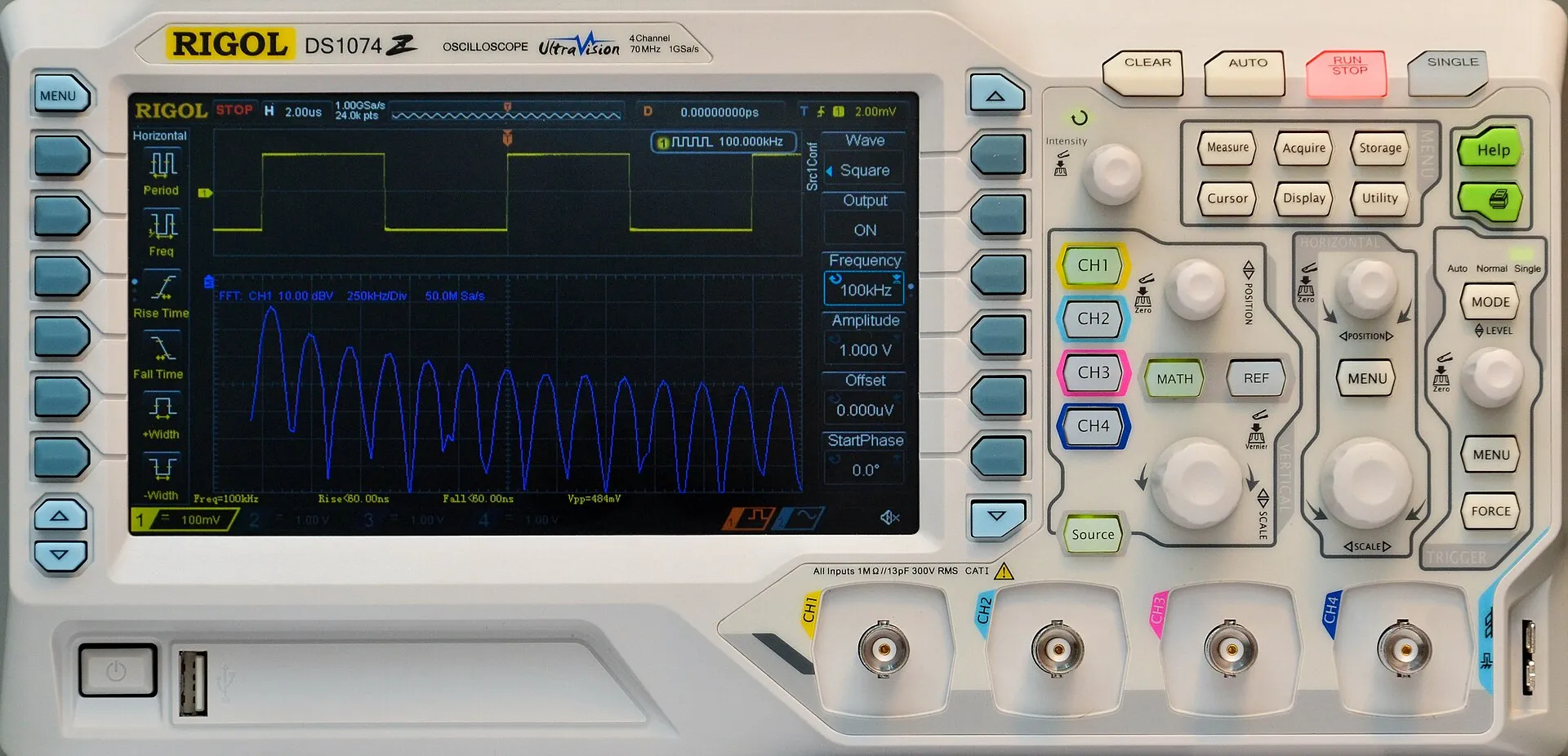 Oscilloscopio digitale da banco bianco, con lo schermo che mostra in giallo un'onda quadra e in blu il suo spettro, i tasti dei menu ai lati dello schermo, manopole e pulsanti a destra e quattro connettori di ingresso in basso.